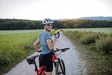 Diabetische Radfahrerin mit einem kontinuierlichen Blutzuckermessgerät am Arm, die während ihrer Radtour Wasser trinkt, um ihren Diabetes während des Trainings in den Griff zu bekommen. Konzept von Bewegung und Diabetes. - HPIF33451