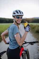 Diabetische Radfahrerin mit einem kontinuierlichen Blutzuckermessgerät am Arm, die während ihrer Radtour Wasser trinkt, um ihren Diabetes während des Trainings in den Griff zu bekommen. Konzept von Bewegung und Diabetes. - HPIF33452