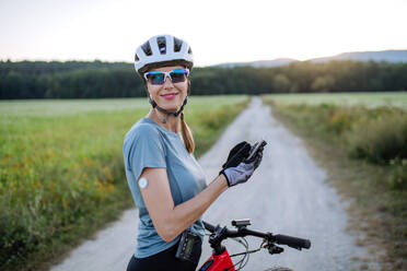 Diabetische Radfahrerin mit kontinuierlichem Blutzuckermessgerät, die ihre Blutzuckerwerte in Echtzeit auf dem Smartphone kontrolliert. Konzept von Bewegung und Diabetes. - HPIF33454