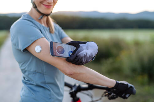 Diabetische Radfahrerin, die ihr Smartphone mit einem kontinuierlichen Blutzuckermessgerät verbindet, um ihren Blutzuckerspiegel in Echtzeit zu überwachen. Konzept von Bewegung und Diabetes. - HPIF33457