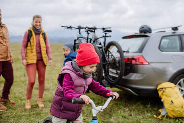 Junge Familie mit kleinen Kindern, die sich auf eine Fahrradtour in der Natur vorbereitet, indem sie die Fahrräder von den Autoträgern abstellt. Konzept der gesunden Lebensweise und der Bewegung. - HPIF33472