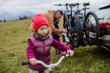 Junges Mädchen, das sich auf eine Fahrradtour in der Natur freut. Der Vater stellt die Fahrräder von den Autoständern ab. Konzept der gesunden Lebensweise und der Bewegung. - HPIF33473
