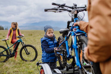 Junge Familie mit kleinen Kindern, die sich auf eine Fahrradtour in der Natur vorbereitet, indem sie die Fahrräder von den Autoträgern abstellt. Konzept der gesunden Lebensweise und der Bewegung. - HPIF33477