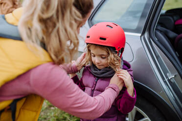 Mother putting on protective helmet on head of her daughter. Young family with little children preparing for bicycle ride in nature. Concept of healthy lifestyle and moving activity. - HPIF33482