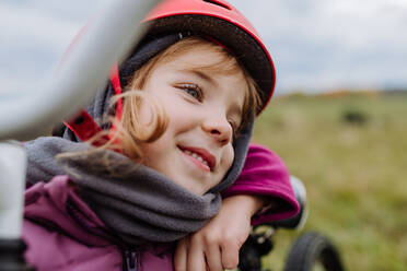 Porträt eines glücklichen kleinen Mädchens mit Helm auf dem Fahrrad. - HPIF33487