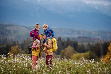 Glückliche Eltern mit ihren kleinen Kindern auf dem Huckepack bei einem Herbstspaziergang inmitten der farbenfrohen Natur, Konzept einer gesunden Lebensweise. - HPIF33503