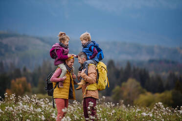 Glückliche Eltern mit ihren kleinen Kindern auf dem Huckepack bei einem Herbstspaziergang inmitten der farbenfrohen Natur. Konzept einer gesunden Lebensweise. Kinder auf den Schultern während der Wanderung tragen. - HPIF33504