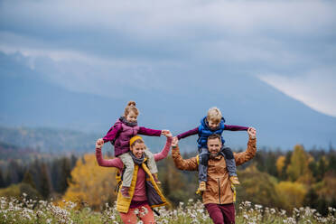 Happy parents with their little kids on piggyback at autumn walk, in the middle of colourfull nature. Concept of a healthy lifestyle. Carrying children on shoulders during the hike. - HPIF33505