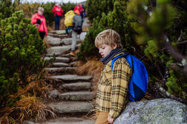 Porträt eines müden Jungen, der sich während einer anstrengenden Wanderung in den herbstlichen Bergen ausruht. Wandern mit kleinen Kindern in schwierigem Gelände. - HPIF33514
