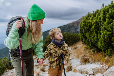 Aktive Mutter und kleiner Sohn mit Trekkingstöcken wandern zusammen in einem herbstlichen Gebirge. Wandern mit kleinen Kindern. - HPIF33523