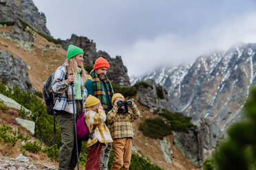 Porträt einer glücklichen Familie, die gemeinsam in den herbstlichen Bergen wandert. Wandern mit kleinen Kindern. Kleiner Junge schaut durch ein Fernglas. - HPIF33531