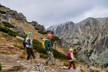 Porträt einer glücklichen Familie mit Trekkingstöcken, die zusammen in einem herbstlichen Gebirge wandern. Wandern mit kleinen Kindern. Familienwanderer, die den Berg hinuntergehen. - HPIF33532
