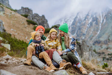 Porträt einer glücklichen Familie, die sich während einer langen Wanderung in den herbstlichen Bergen ausruht. Wandern mit kleinen Kindern. Kleiner Junge schaut durch ein Fernglas. - HPIF33538