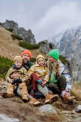 Happy family sitting and resting, during hiking together in an autumn mountains. - HPIF33539