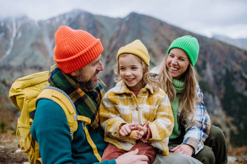 Eine glückliche Familie, die sich ausruht, einen Snack zu sich nimmt und die Aussicht beim gemeinsamen Wandern in den herbstlichen Bergen genießt. Mutter, Vater und Tochter auf einer kinderfreundlichen Wanderung. - HPIF33541