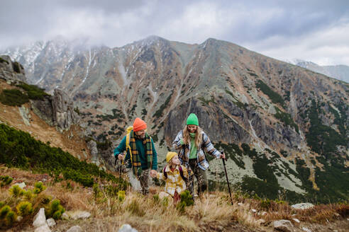 Porträt einer glücklichen dreiköpfigen Familie mit Trekkingstöcken, die gemeinsam in den herbstlichen Bergen wandern, mit kleinen Kindern. - HPIF33543