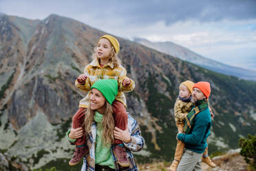 Porträt einer glücklichen Familie, die gemeinsam in den herbstlichen Bergen wandert. Wandern mit kleinen Kindern. Mutter trägt junges Mädchen auf den Schultern. - HPIF33549
