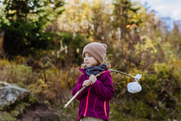 Portrait of little girl with bindle during autumn hike in mountains. Girl holding stick with cloth carrying snack inside. - HPIF33561