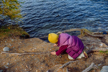 Little girl playing on the shore of the lake in mountains. Girl tourist resting near the lake, having fun and playing with pebbles. - HPIF33568