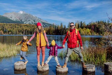 Happy young family with two little children, standing on wooden steps on the shore of the lake in mountains. - HPIF33569