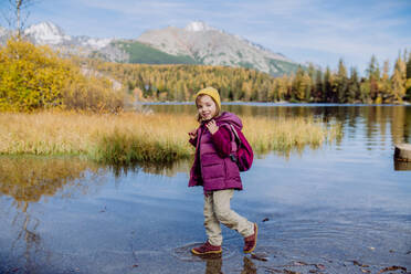 Little girl walking in shore of lake, in the middle of beautiful autumn nature. - HPIF33572