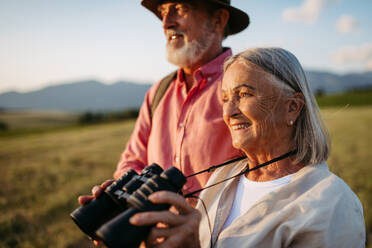 Portrait of a senior woman looking through binoculars. Senior couple walking through the autumn nature. Elderly spouses going mushroom picking. - HPIF33584