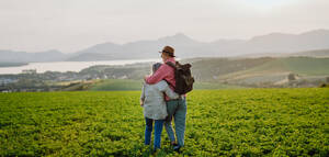 Älteres Paar steht in der Mitte einer Wiese und hat einen romantischen Moment in der herbstlichen Natur. Ältere Eheleute schauen auf eine ruhige Landschaft und genießen die schöne Aussicht auf die Hohe Tatra. Minimalistische Landschaftsfotografie, Banner mit Kopierraum. - HPIF33586