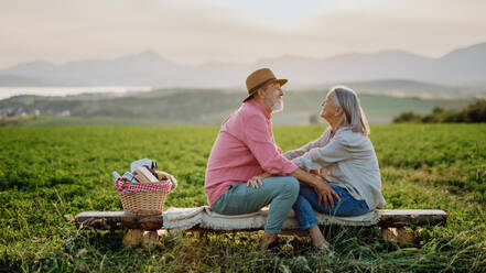 Älteres Paar sitzt auf einer Wiese und hat einen romantischen Moment in der herbstlichen Natur. Ältere Eheleute schauen sich an, mit der ruhigen Landschaft der Hohen Tatra im Hintergrund. - HPIF33590