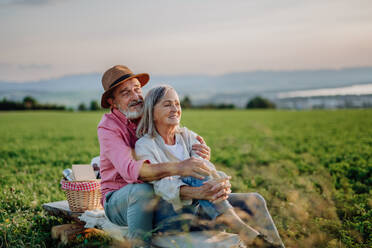 Umarmendes älteres Paar, das den Sonnenuntergang in der herbstlichen Natur beobachtet und ein Picknick macht. - HPIF33593