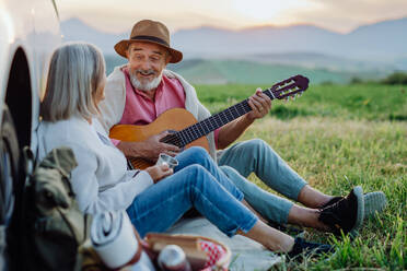 Potrait eines älteren Ehepaars, das nach einer langen Autofahrt im Auto sitzt und Gitarre spielt. Ältere Eheleute genießen bei einem Roadtrip die ruhige Landschaft der Hohen Tatra hinter sich. - HPIF33603