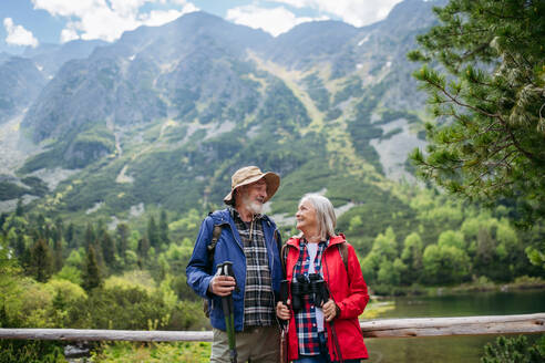 Aktives älteres Ehepaar beim gemeinsamen Wandern in den herbstlichen Bergen, auf einem seniorenfreundlichen Weg. Ältere Eheleute im Urlaub in den Bergen, die ihren Jahrestag feiern. Ältere Touristen mit Rucksäcken, die Trekkingstöcke für Stabilität benutzen. - HPIF33608