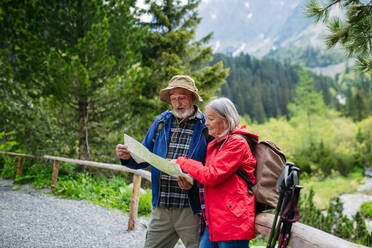 Active elderly couple hiking together in autumn mountains, on senior friendly trail. Senior spouses on the vacation in the mountains celebrating anniversary. Senior tourists with backpacks reading map, preparing for hike. - HPIF33609