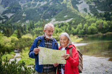 Active elderly couple hiking together in autumn mountains, on senior friendly trail. Senior spouses on the vacation in the mountains celebrating anniversary. Senior tourists with backpacks reading map, preparing for hike. - HPIF33610