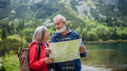 Active elderly couple hiking together in autumn mountains, on senior friendly trail. Senior spouses on the vacation in the mountains celebrating anniversary. Senior tourists with backpacks reading map, preparing for hike. - HPIF33613