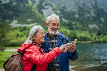 Aktives älteres Ehepaar beim gemeinsamen Wandern in den herbstlichen Bergen, auf einem seniorenfreundlichen Weg. Mann und Frau schauen auf eine Karte auf einem Smartphone und suchen einen Wanderweg. - HPIF33617