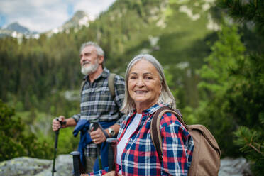 Potrait einer aktiven älteren Frau, die mit ihrem Mann in den herbstlichen Bergen auf einem seniorenfreundlichen Wanderweg wandert. Ein älterer Tourist mit Rucksack, der Trekkingstöcke zur Stabilität benutzt. - HPIF33622