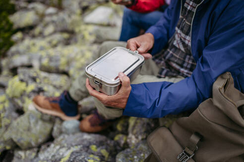 Close up of snack in lunchbox during hike. Couple of turists having healthy snack, to get energy . - HPIF33630