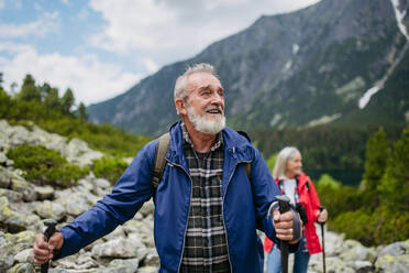 Potrait eines aktiven älteren Mannes, der mit seiner Frau in den herbstlichen Bergen auf einem seniorenfreundlichen Wanderweg wandert. Ein älterer Tourist mit Rucksack, der Trekkingstöcke zur Stabilität benutzt. - HPIF33640
