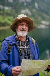 Potrait eines aktiven älteren Mannes beim Wandern in den herbstlichen Bergen, auf einem seniorenfreundlichen Wanderweg. Ein älterer Tourist mit Rucksack sucht seinen Wanderweg auf einer Papierkarte, - HPIF33654