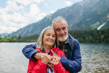 Porträt eines schönen aktiven älteren Paares, das gemeinsam in den herbstlichen Bergen wandert. Ältere Eheleute im Urlaub in den Bergen, die ihren Jahrestag feiern. Ältere Touristen, die sich gegenseitig vor einem See umarmen. - HPIF33673