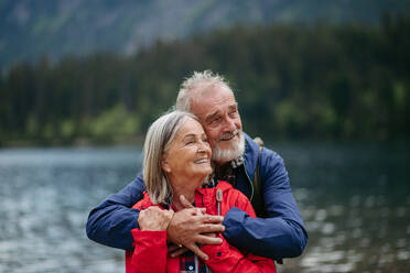 Porträt eines schönen aktiven älteren Paares, das zusammen in den herbstlichen Bergen wandert. Ältere Ehepartner im Urlaub in den Bergen, die ihren Jahrestag feiern. Ältere Touristen, die sich gegenseitig vor einem See umarmen. - HPIF33675