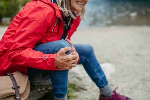 Ältere Frau verletzt sich beim Wandern in den Bergen am Bein. Touristin kommt vom Weg ab und stürzt. Ältere Touristin verspürt Schmerzen unter der Kniescheibe, auch bekannt als Wandererknie. - HPIF33676