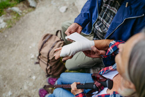 Älterer Mann hilft verletzter Touristin. Eine ältere Frau verletzte sich beim Wandern in den Bergen am Arm. Die Touristin kam vom Weg ab und stürzte. - HPIF33681