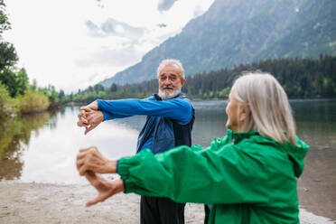 Ein älteres Ehepaar macht im Herbst Yoga, Tai Chi und Pilates am See. Ein älteres Ehepaar verbringt seinen Aktivurlaub in den Bergen und genießt die Kombination aus körperlicher Aktivität und Entspannung. Rentner dehnen sich nach dem Training im Freien - HPIF33685