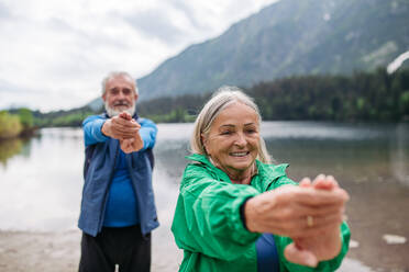 Ein älteres Ehepaar macht im Herbst Yoga, Tai Chi und Pilates am See. Ein älteres Ehepaar verbringt seinen Aktivurlaub in den Bergen und genießt die Kombination aus körperlicher Aktivität und Entspannung. Rentner dehnen sich nach dem Training im Freien - HPIF33686