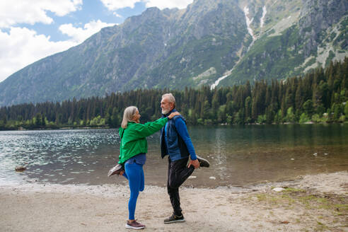 Ganzkörperaufnahme eines älteren Paares, das im Herbst am See Yoga, Tai Chi und Pilates macht. Ein älteres Ehepaar verbringt seinen Aktivurlaub in den Bergen und genießt die Kombination aus körperlicher Aktivität und Entspannung. Rentner dehnen sich nach dem Training im Freien - HPIF33688