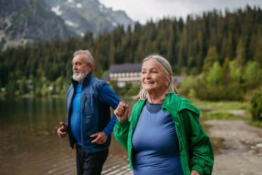 Senior couple running by the lake in the autumn. Elderly husband and wife spending active vacation in the mountains, enjoying combination of physical activity and relaxation. - HPIF33689