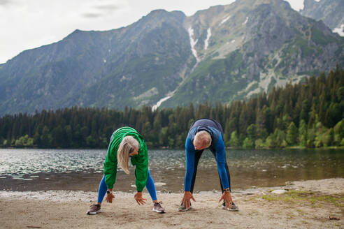 Ein älteres Ehepaar macht im Herbst Yoga, Tai Chi und Pilates am See. Ein älteres Ehepaar verbringt seinen Aktivurlaub in den Bergen und genießt die Kombination aus körperlicher Aktivität und Entspannung. Rentner dehnen sich nach dem Training im Freien - HPIF33692