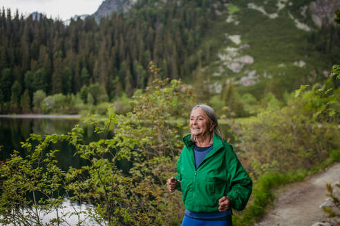 Ältere Läuferin, die im Herbst am See läuft. Ältere Frau, die einen aktiven Urlaub in den Bergen verbringt und die Kombination aus körperlicher Aktivität und Entspannung genießt. - HPIF33698