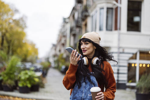 Woman wearing knit hat and sending voicemail through smart phone - JCCMF10933